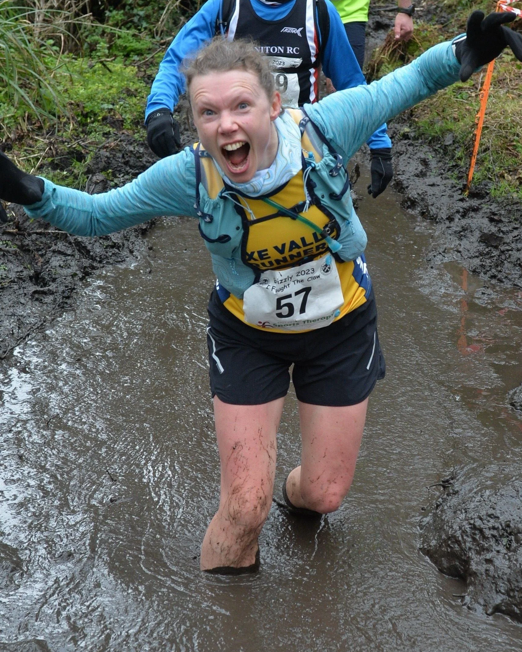 An extremely muddy Katharine wading through a knee-deep bog and roaring like a bear at the camera during the Grizzly trail running race