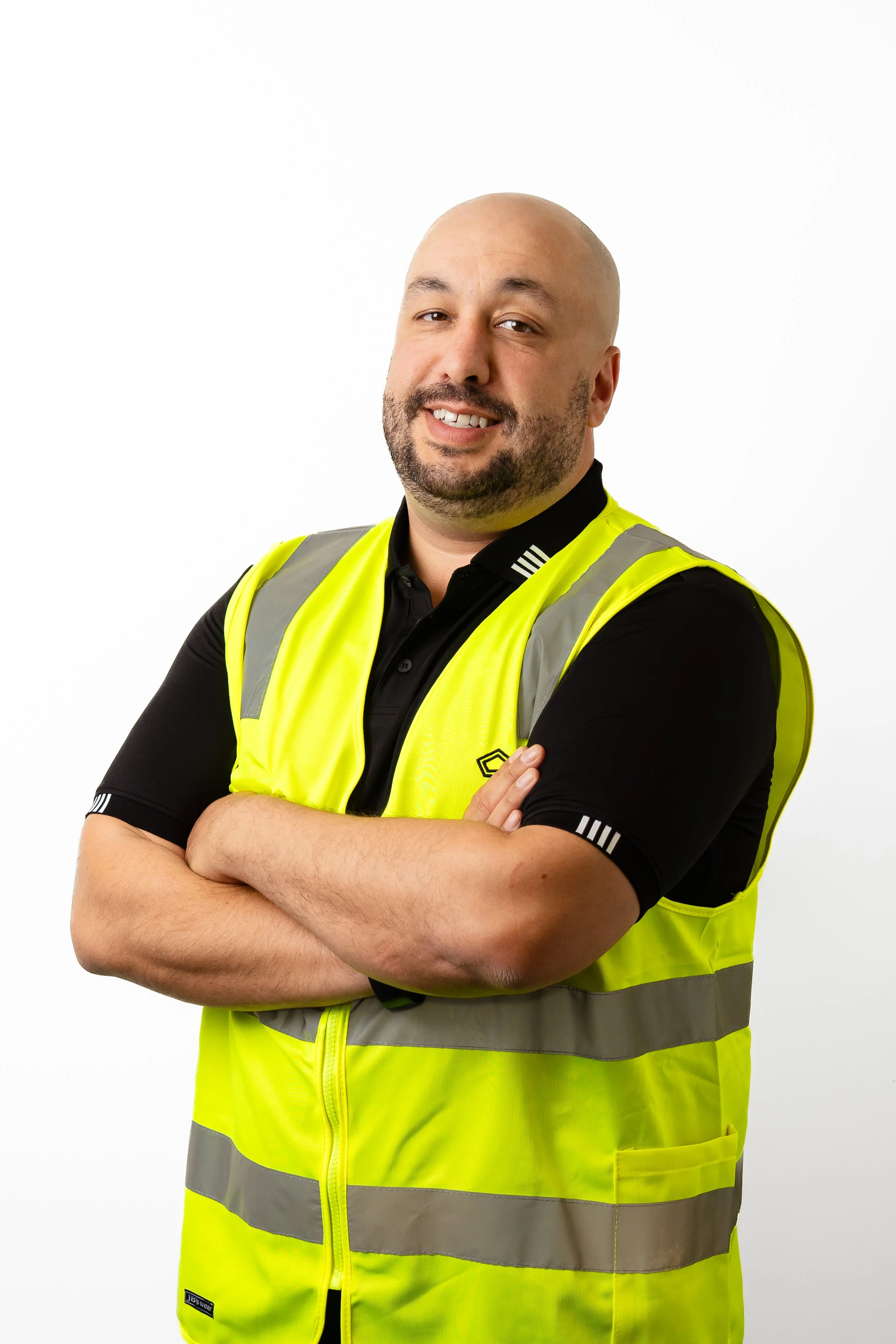 A smiling man with dark hair and a beard wearing a dark blue button-up shirt standing against a plain white wall.