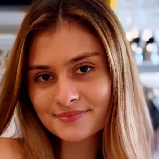 Close-up of a young woman with long, light brown hair smiling gently, indoors with blurred background.