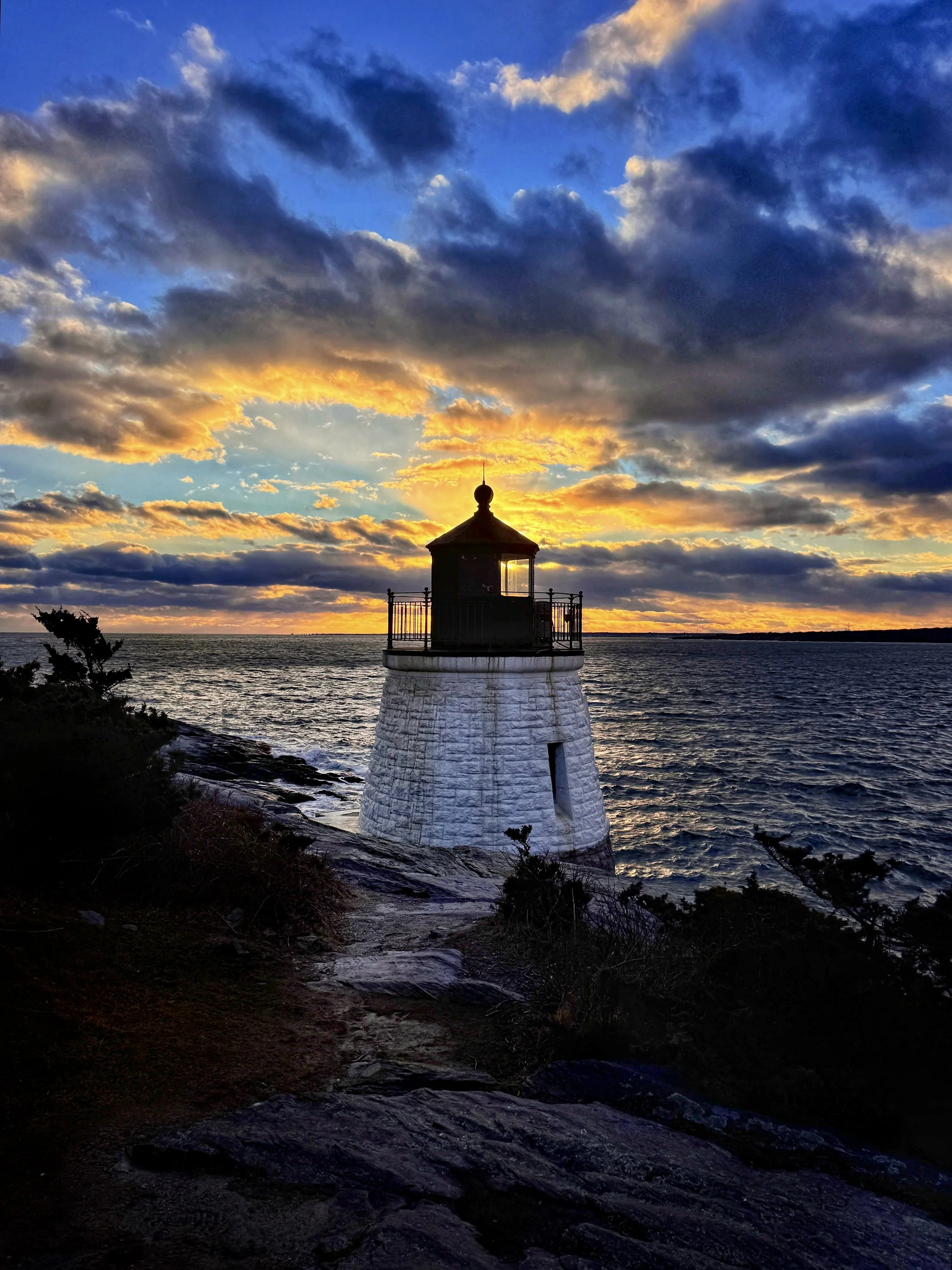 A dramatic orange and blue sunset and cloud sky over Narragansett Bay at Castle Hill Lighthouse in Newport, Rhode Island