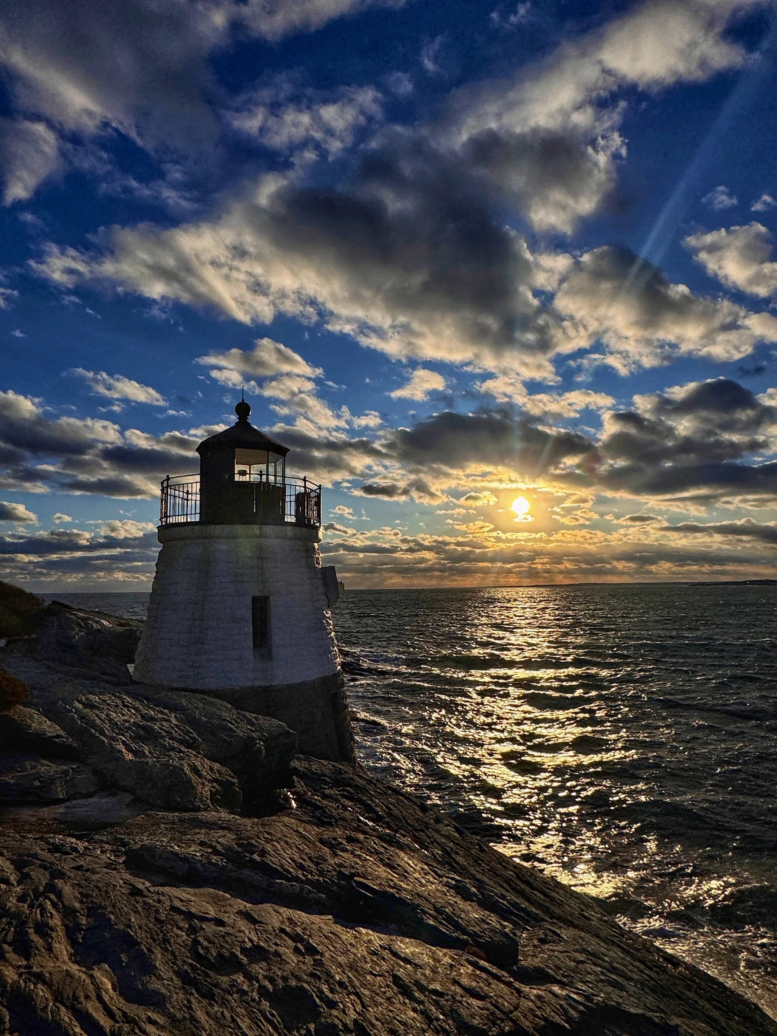 A vibrant golden hour sunset at Castle Hill Lighthouse in Newport, Rhode Island that glimmers on Narragansett Bay