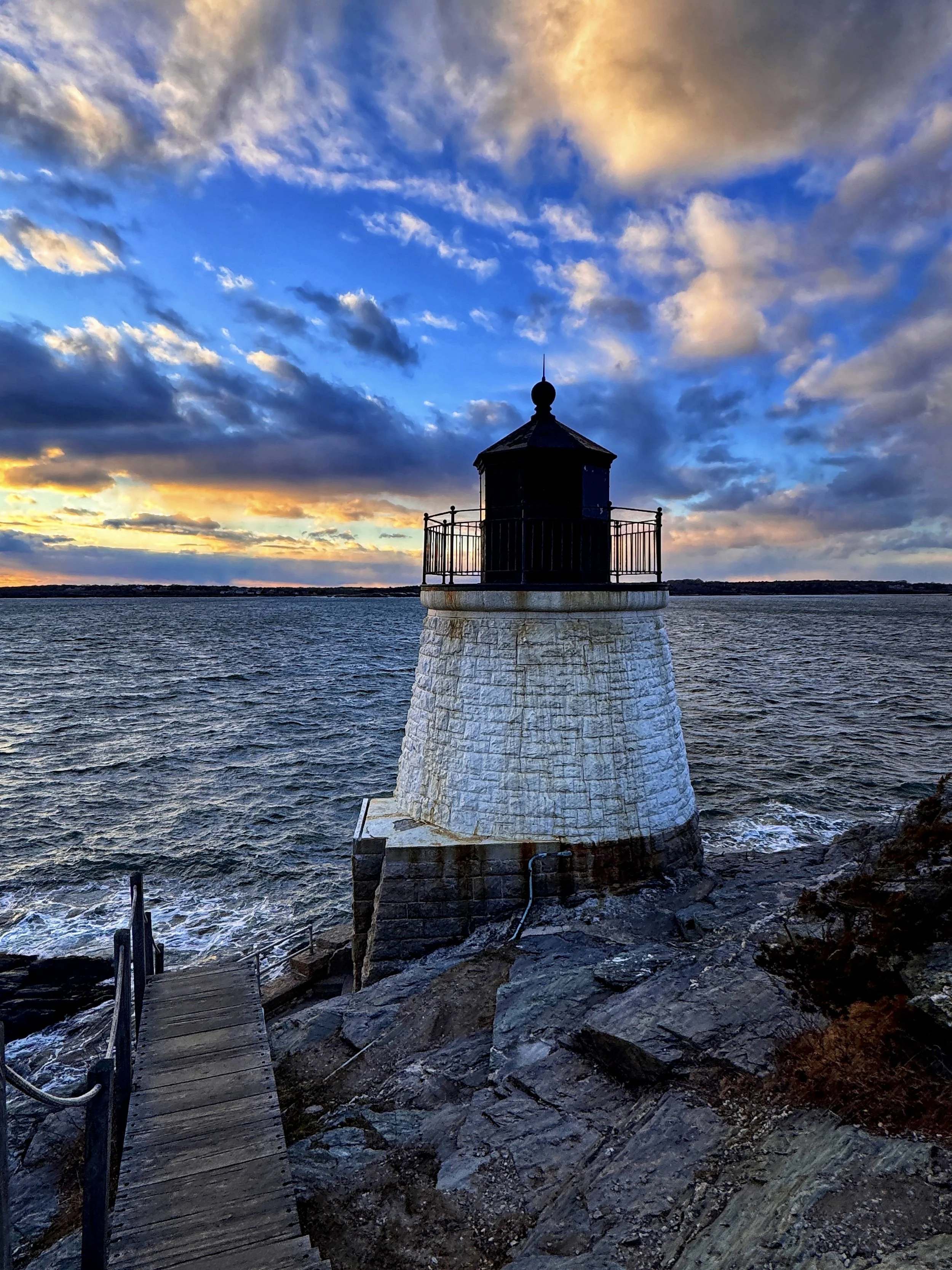 A vibrant sunset cloudsky over Castle Hill Light in Newport, Rhode Island, as seen from the wooden staircase above it