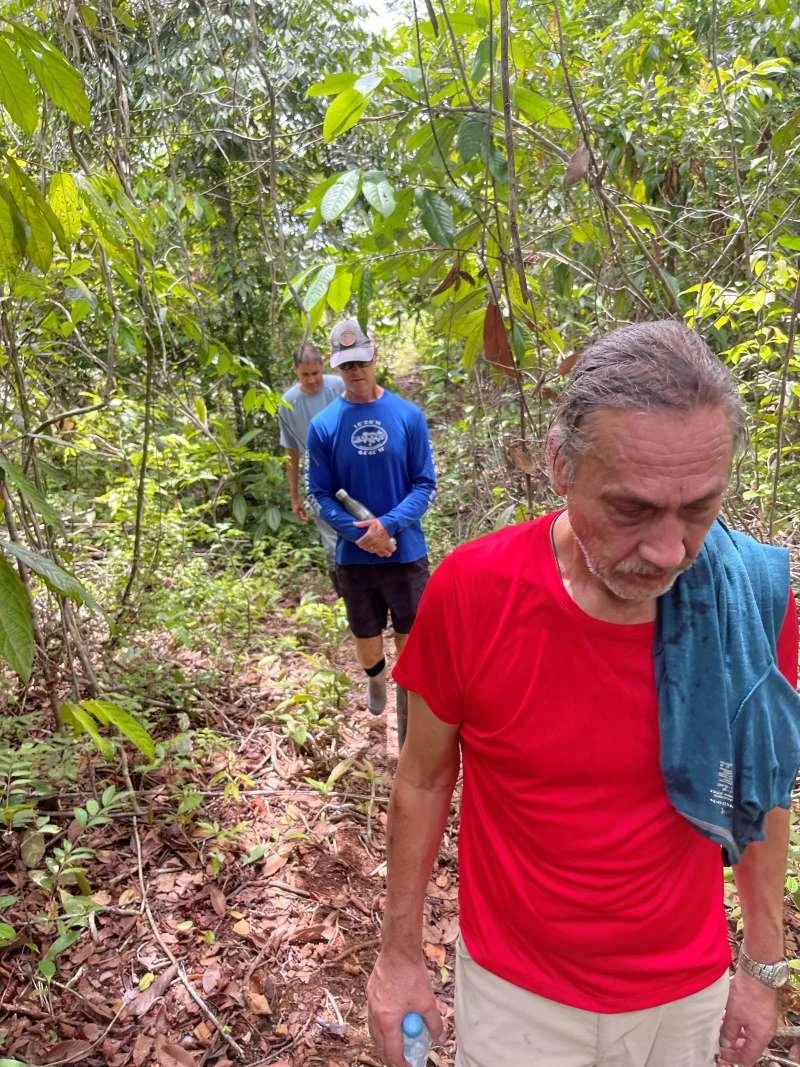 Three plant medicine retreat guests lightly dressed walking through a dense green forest, near Casa del Maestro ayahuasca center in Peru.