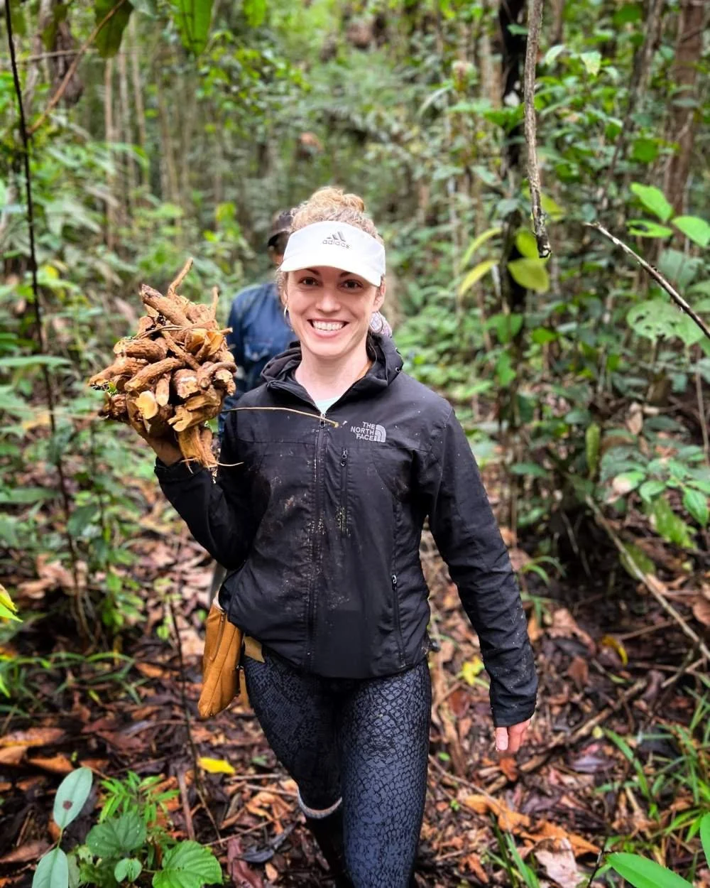 An ayahuasca retreat guest, smiling and holding a cluster of sanango roots in the Amazon jungle.