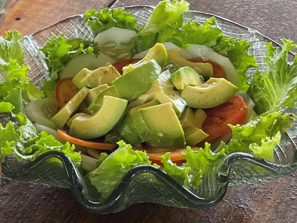 A glass dish with a fresh vegetable salad containing lettuce, sliced tomatoes, cucumber, and avocado, served on a wooden table at an ayahuasca retreat center in Peru.