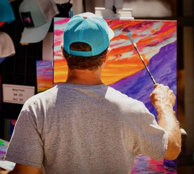Zach Otte painting a vibrant sunset landscape with mountains and a river on a canvas for Casa del Maestro art and ayahuasca retreat.
