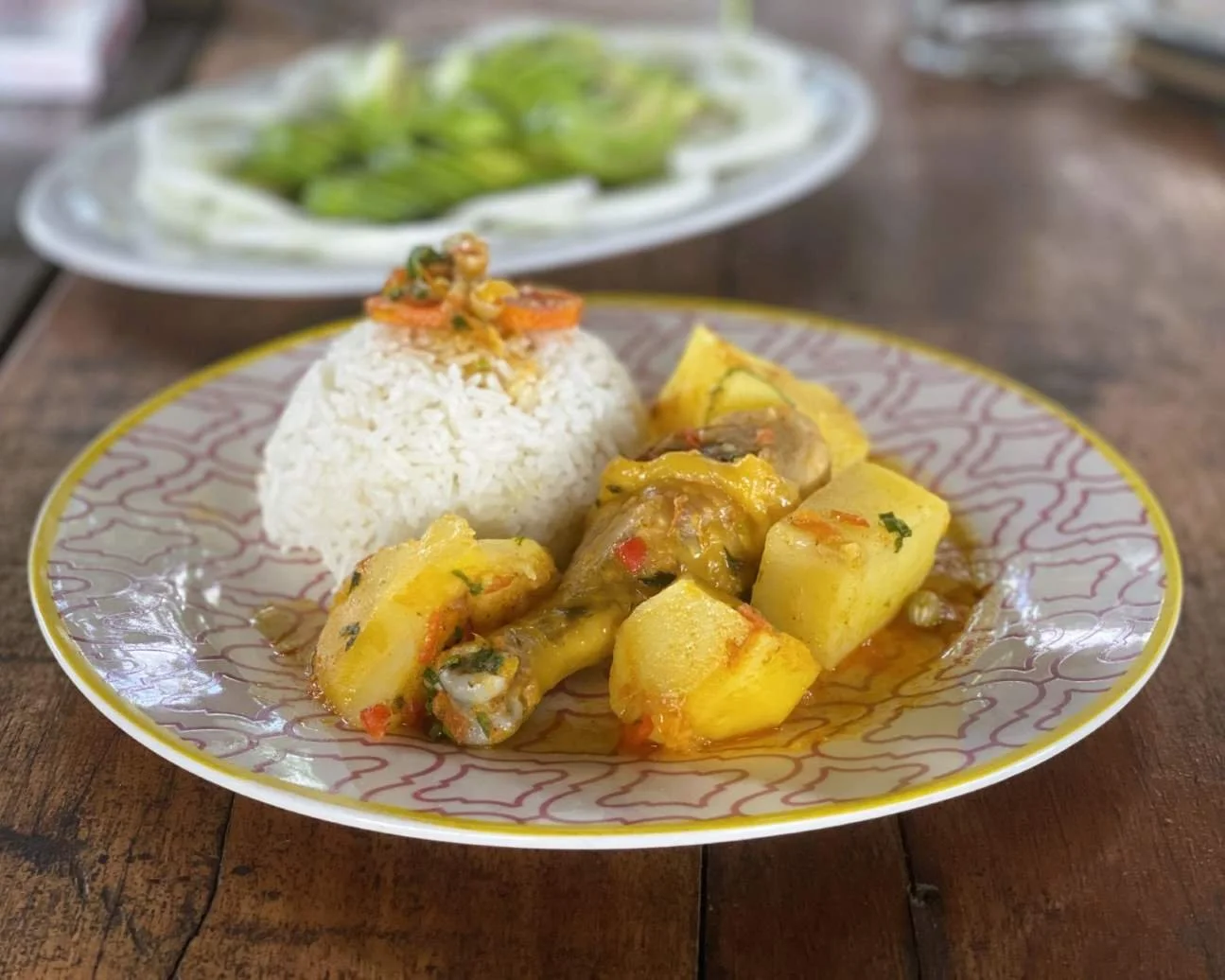 Тарелка риса с овощами и куриным карри, поданная с отварным картофелем, гарниром из зелени и небольшим гарниром из овощей на заднем плане на деревянном столе во время ретрита по растительной медицине.
