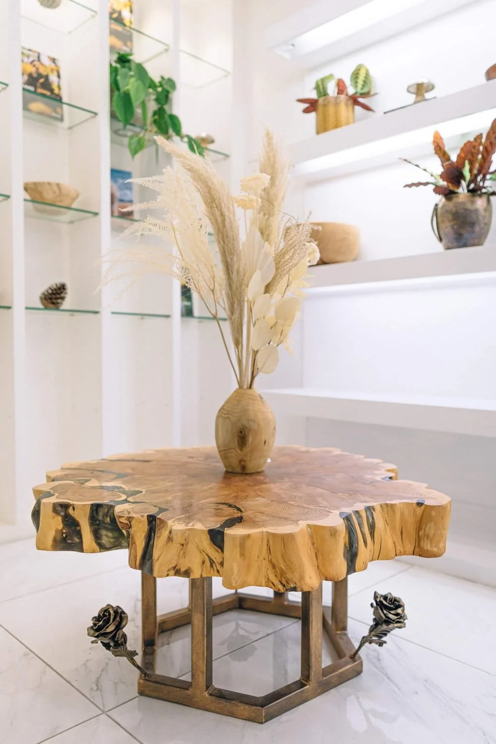 A richly grained yew slab rests on a hexagonal metal base adorned with sculpted roses, blending organic form with quiet elegance — a statement of nature refined through design.