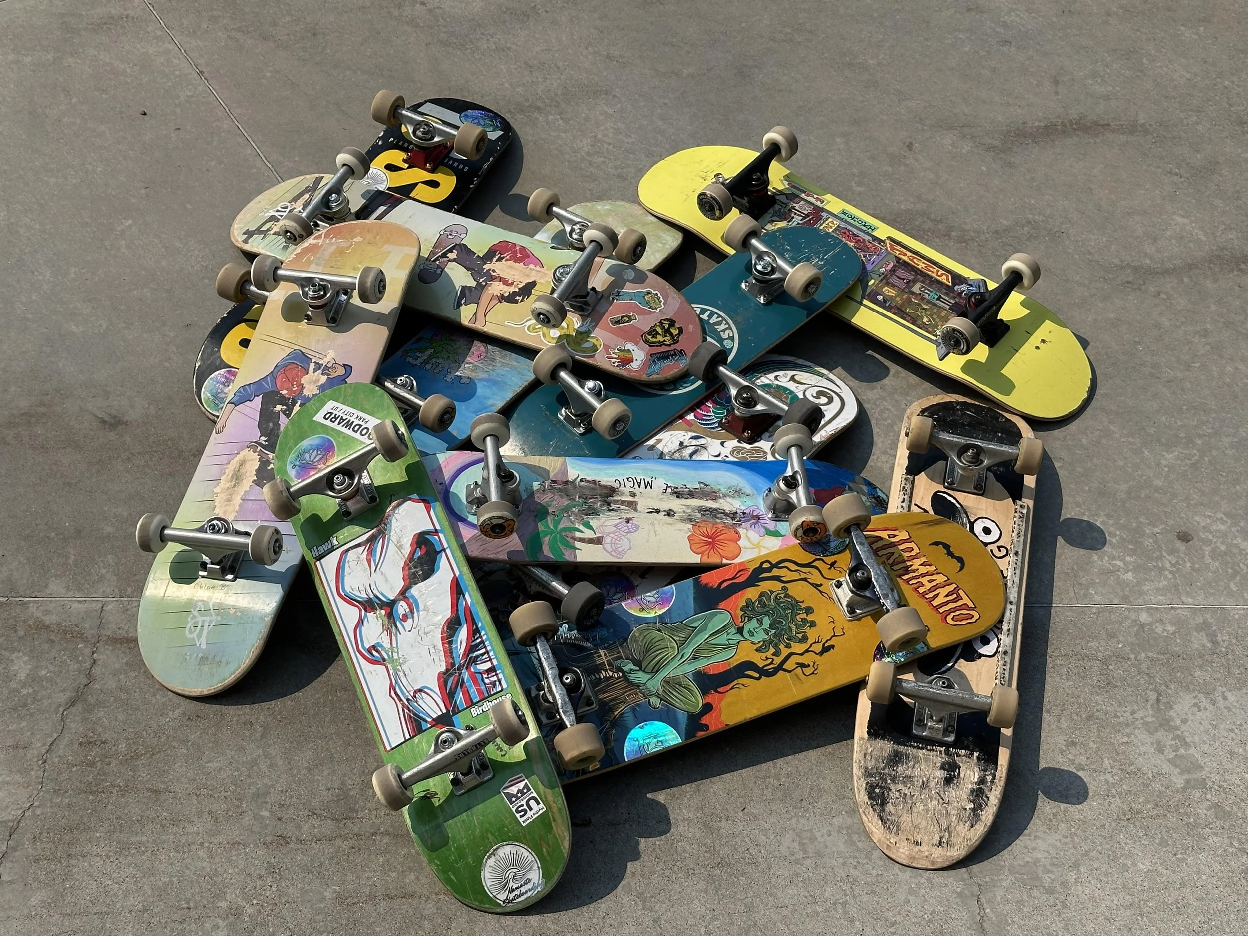 Multiple skateboards with colorful designs, lying on a concrete surface.