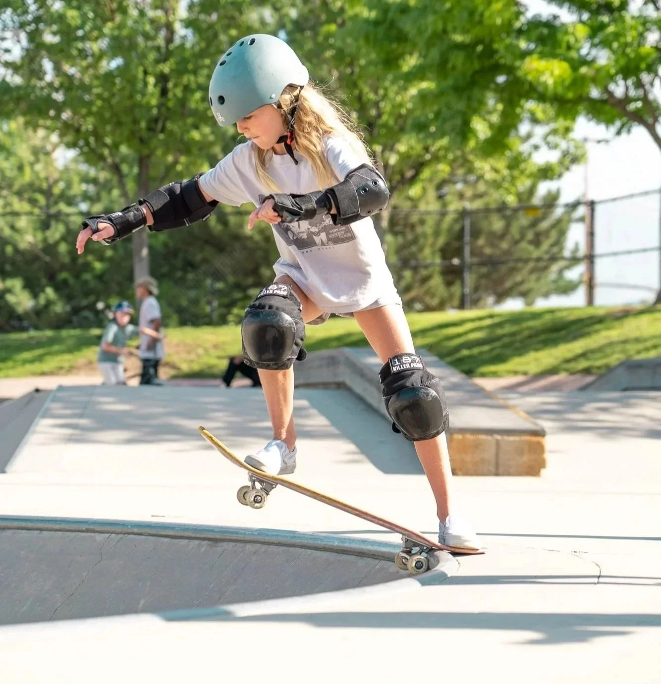 Girl wearing a helmet and knee pads skateboarding at a skate park during the daytime.