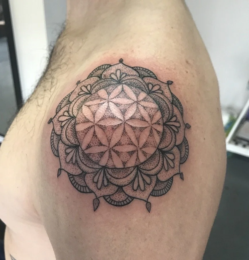 Black geometric mandala tattoo on shoulder and upper arm.