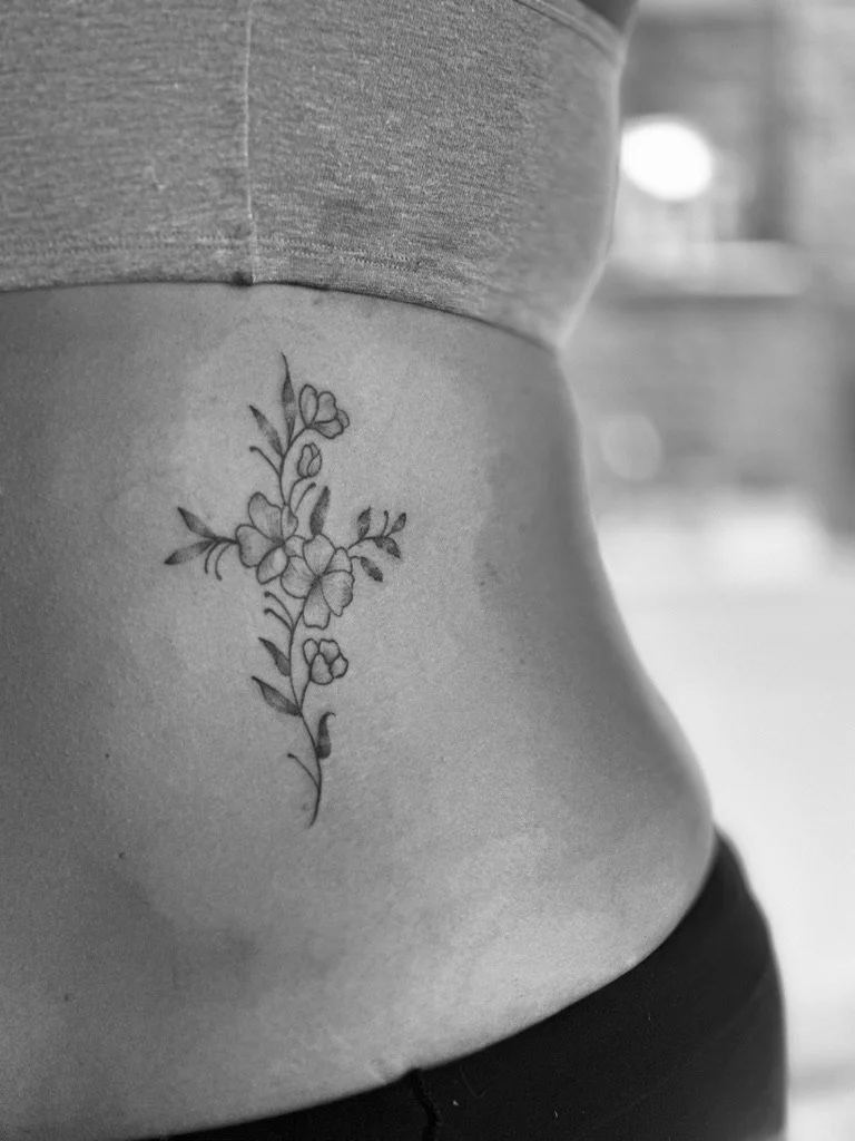 Black and white close-up of a person's side waist with a floral tattoo of a branch with flowers and leaves.