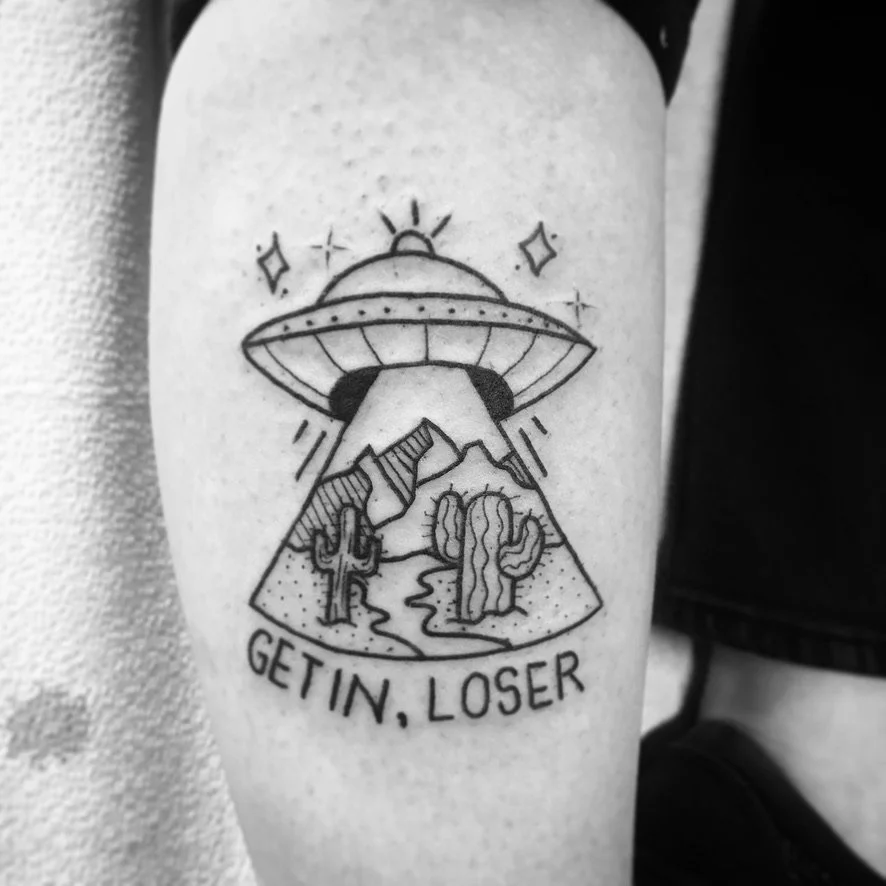 Tattoo of a UFO beaming up mountains and cacti with the text "Get In, Loser."