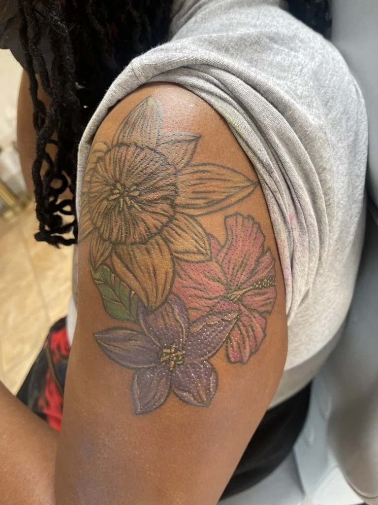 Tattoo of colorful hibiscus flowers and leaves on a Black African American person's upper arm.