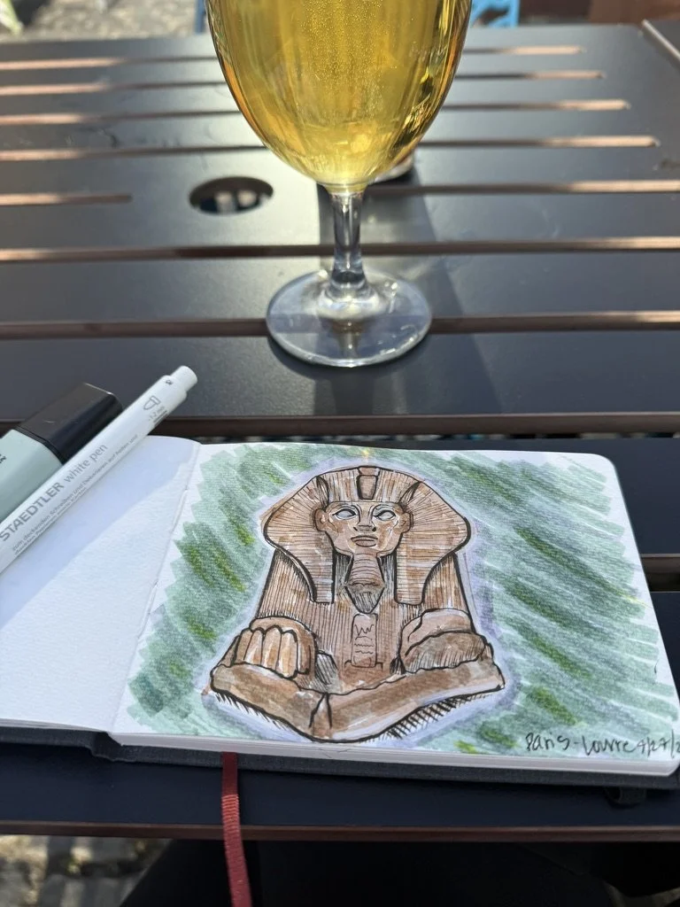 A drawing of a Sphinx statue sketched with brown and black ink, colored with light green background. A glass of white wine is on the table next to the drawing, with a white marker nearby.