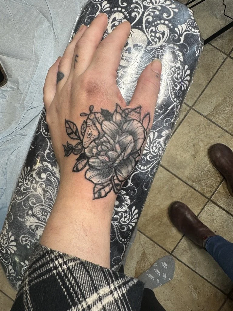 Hand with a cover up tattoo of a detailed rose with leaves on the top of the hand, resting on a decorative black and white surface.
