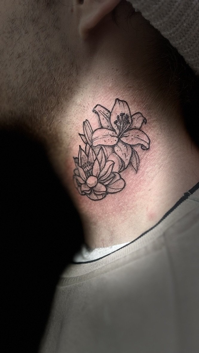 Close-up of a person's neck with a tattoo of lilies and other flowers.
