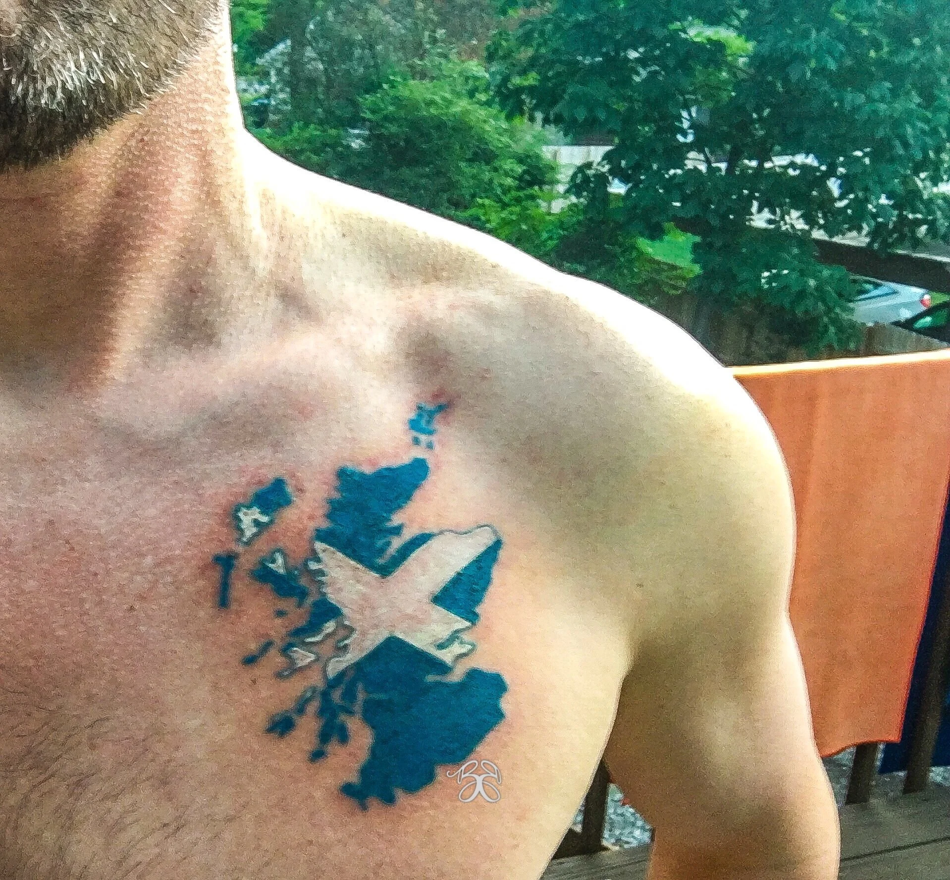 A close-up of a person's shoulder with a tattoo depicting the map Scotland in blue with a white cross over it.