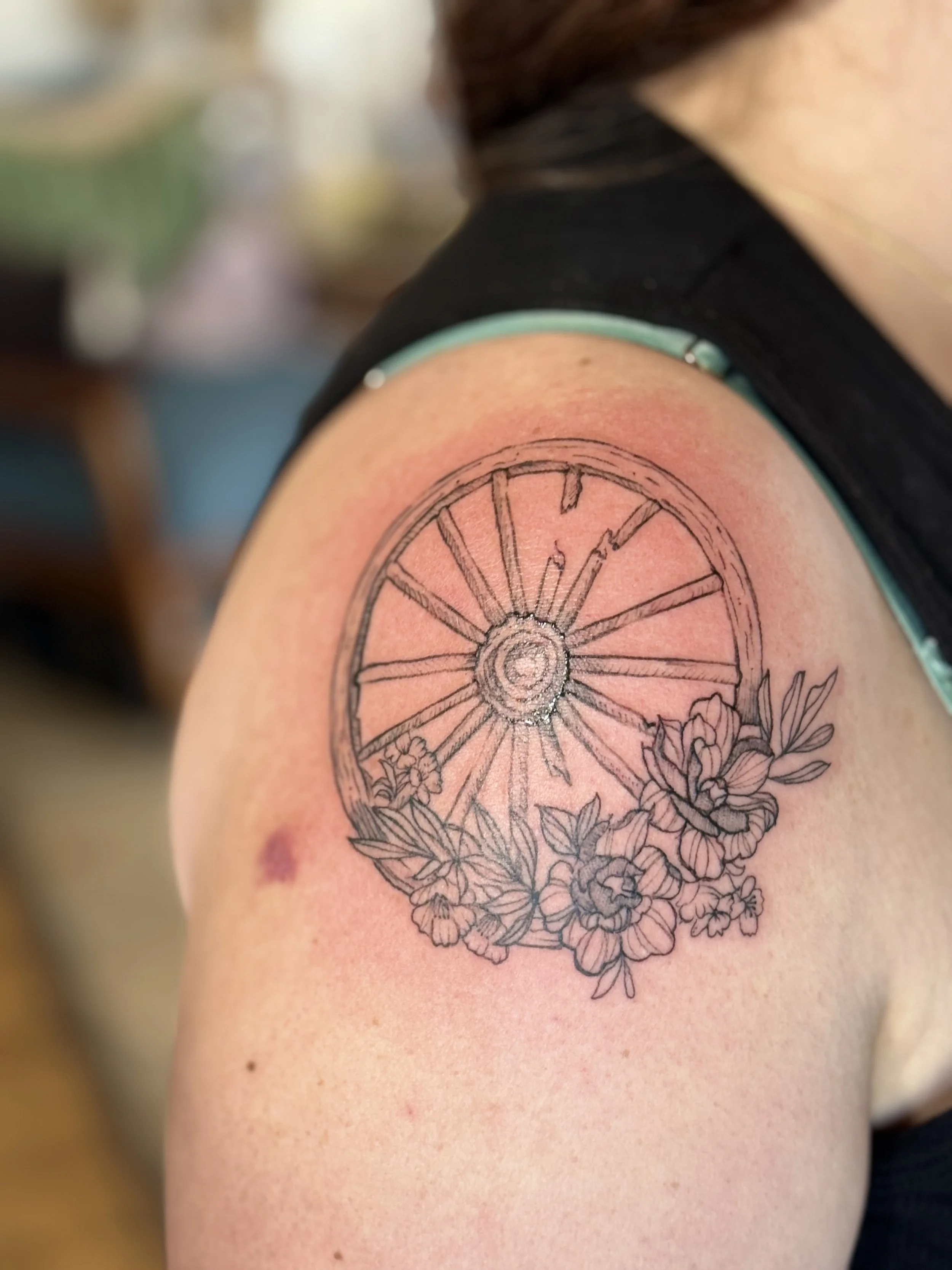 Broken wooden wheel and flowers tattooed on an arm
