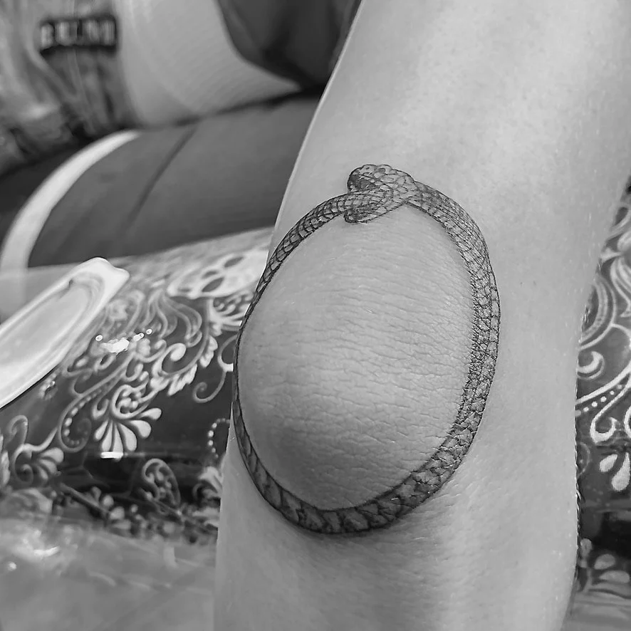 Close-up of a tattoo of a snake coiled around a circular shape on a person's elbow.