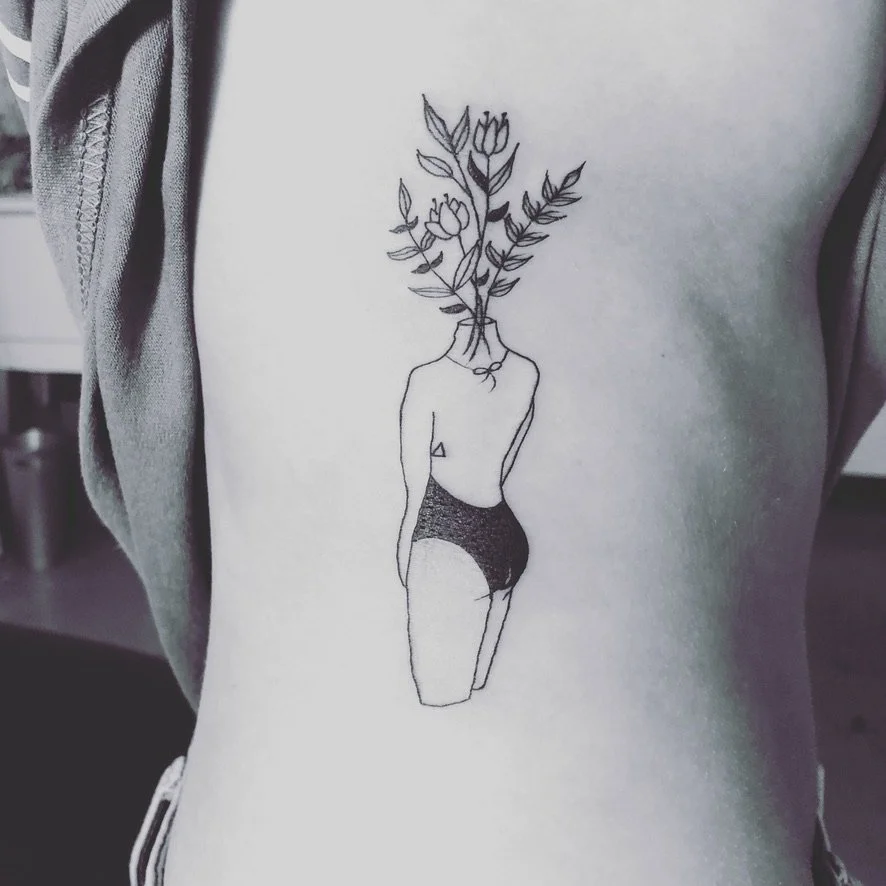 Tattoo of a female figure with a flower bouquet for a head on person's side torso.