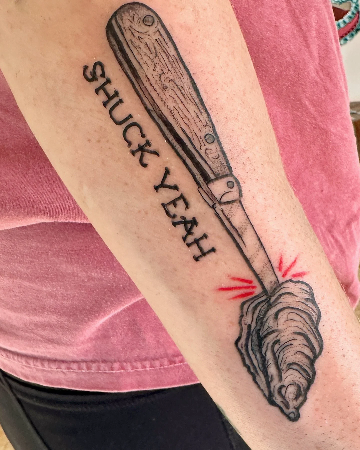 Tattoo of a pocketknife with the words 'SHUCK YEAH' underneath, on a person's arm.