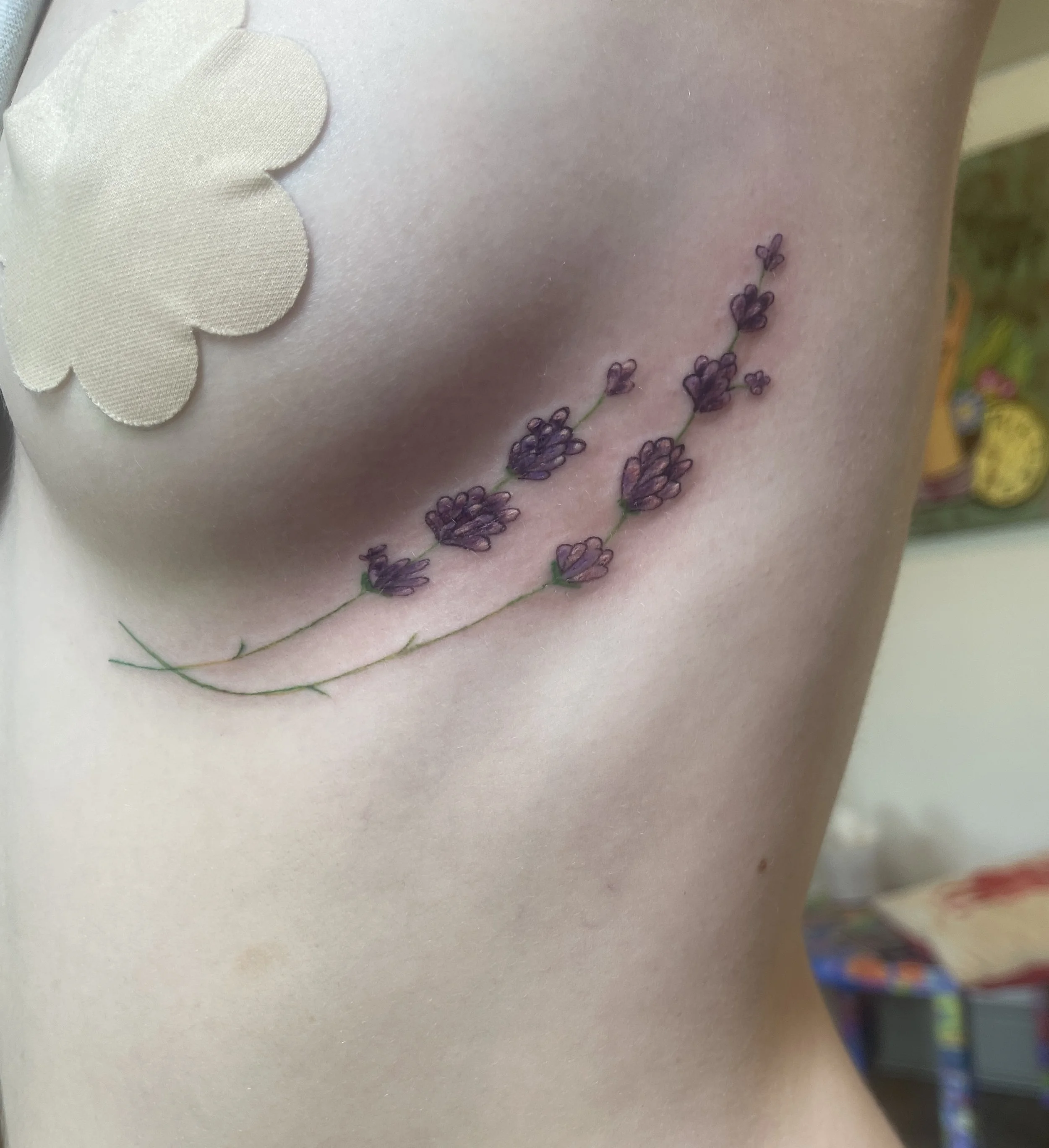 Tattoo of lavender flowers under a woman's breast.