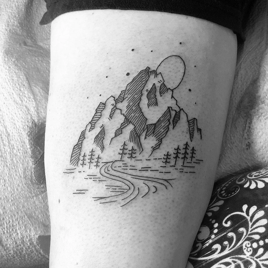 Black and white tattoo of mountains, trees, a winding river, a sun or moon, and stars.