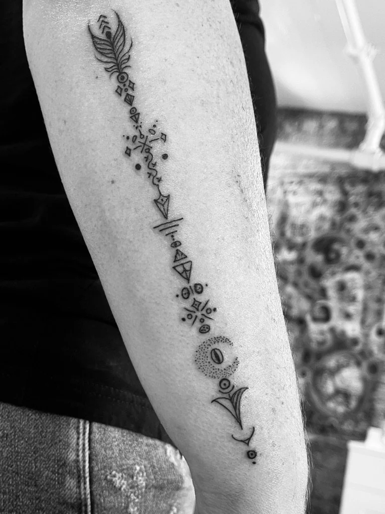 Black and white tattoo on a person's forearm featuring geometric shapes, lines, and a feather at the top.