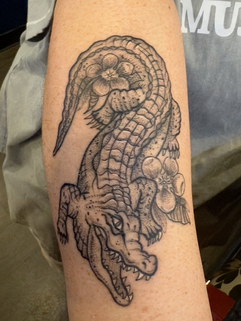 Tattoo of a crocodile with flowers on a person's arm.