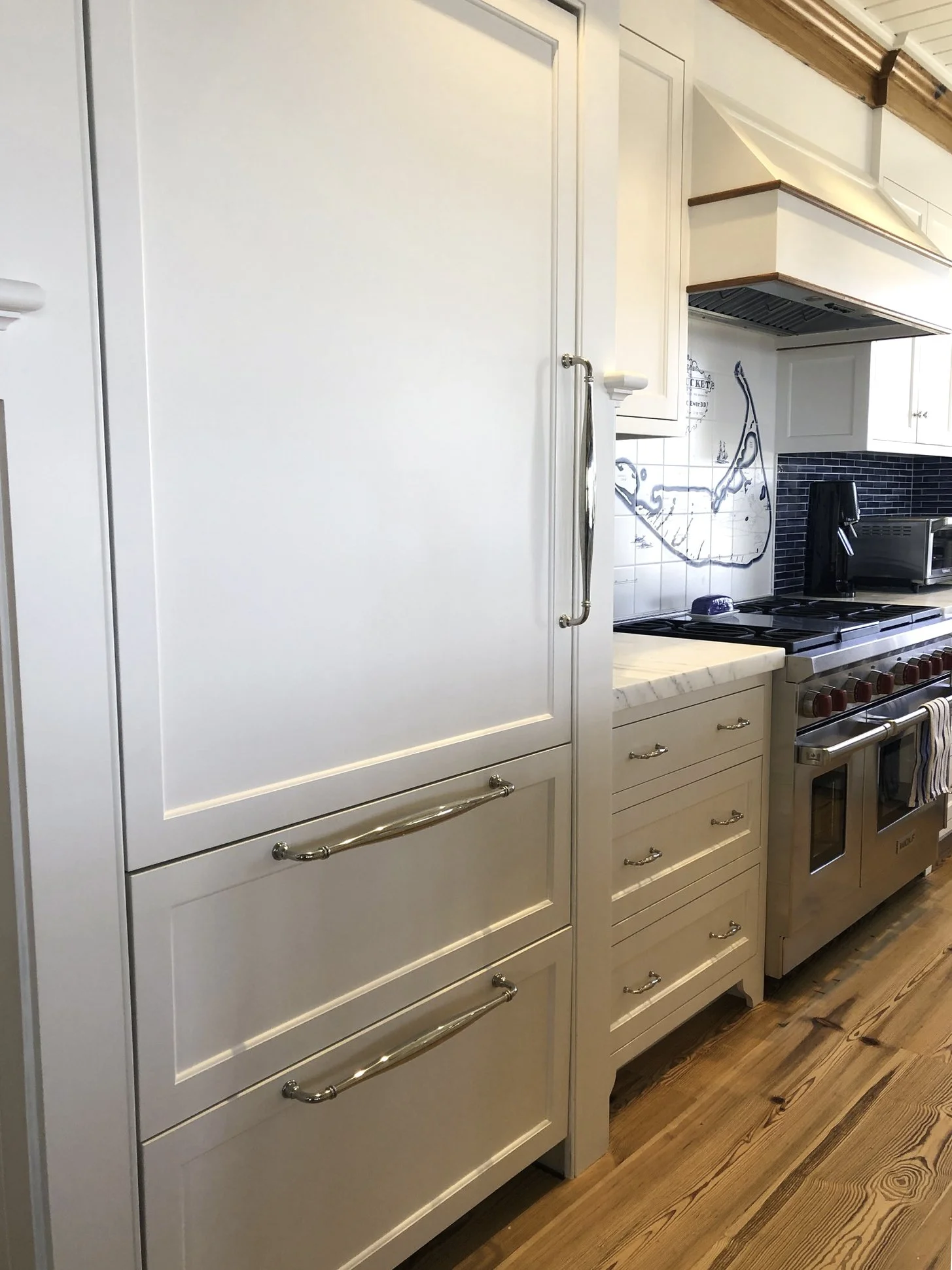 Close-up view of a kitchen with white cabinets, a marble countertop, a black stove, and a blue tile backsplash. Custom Coastal Kitchen, Nantucket custom kitchen, Culbertson Woodworking.