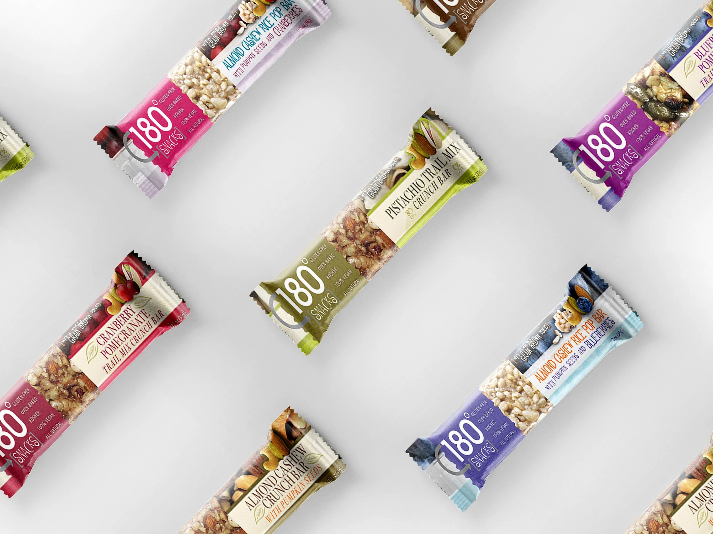 Assorted snack bars with colorful packaging, including almond, pistachio, cranberry, and blueberry flavors, arranged diagonally on a light background.