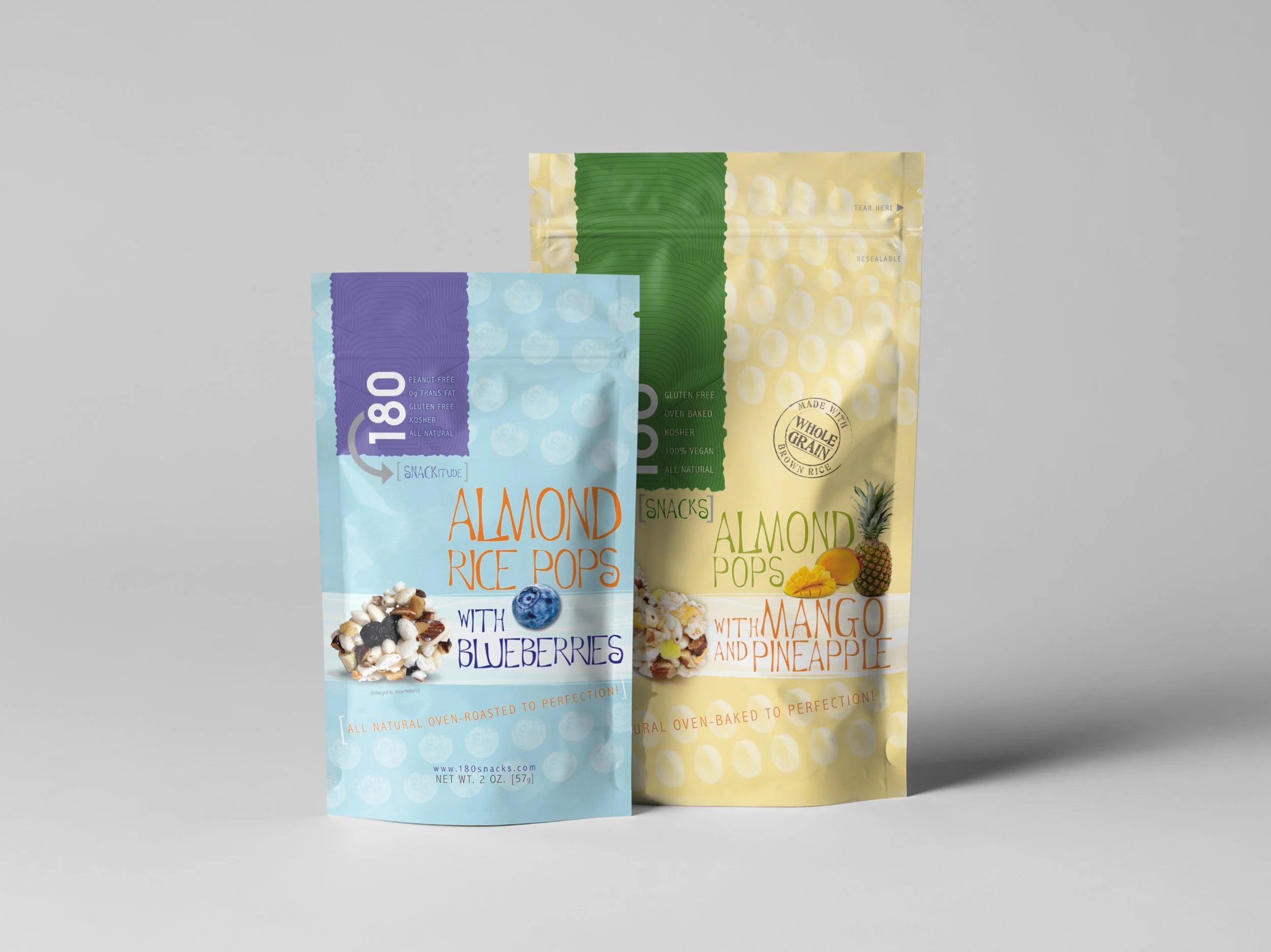 Two bags of almond rice pop snacks, one with blueberries and the other with mango and pineapple, stand against a gray background.