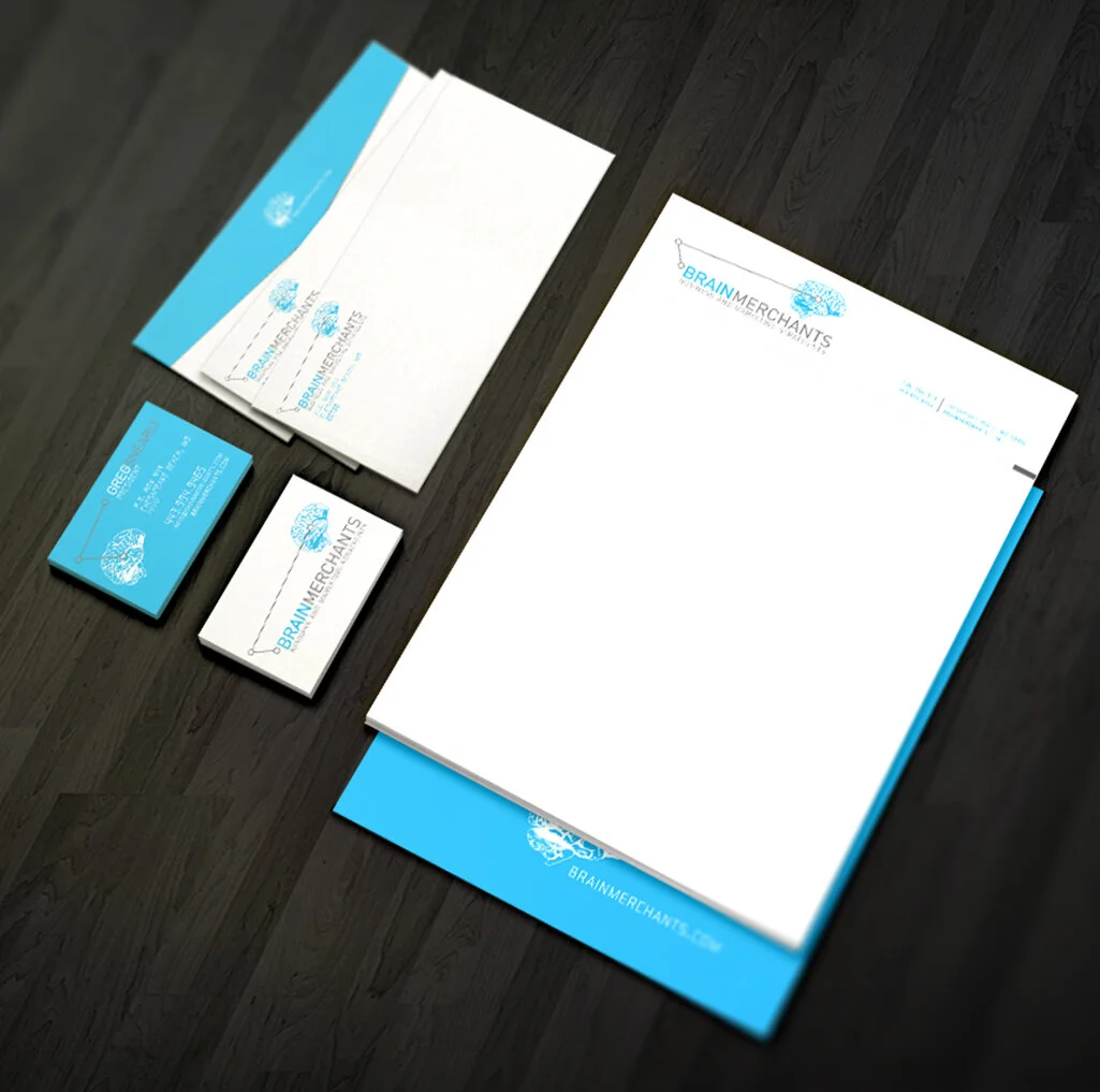 A set of branded business stationery on a dark wooden surface, including letterhead, envelope, business cards, and a folder, all featuring a blue and white logo of a brain above the text 'BRAIN MERCHANTS'.