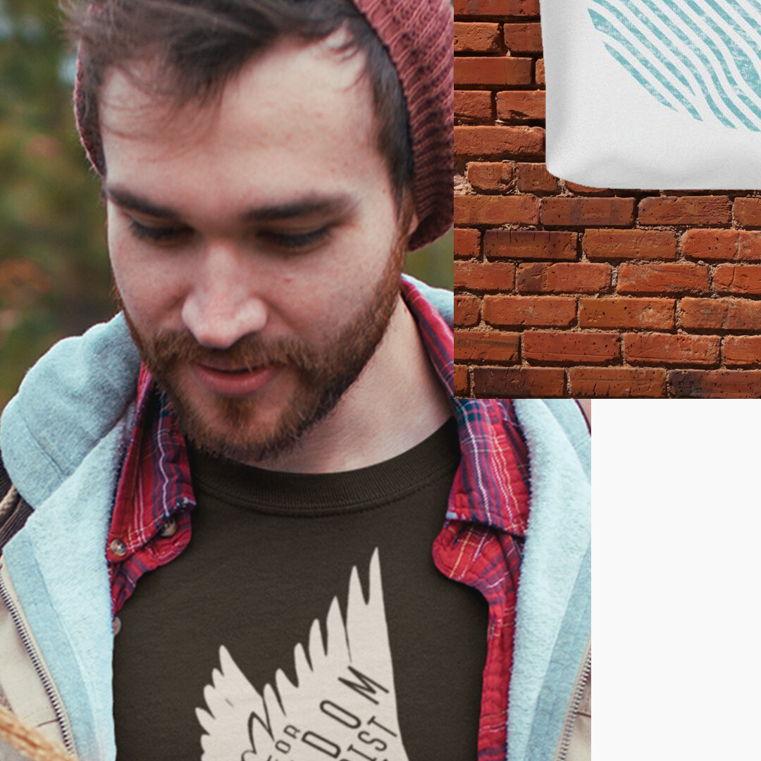 A young man wearing a red beanie, plaid shirt, and gray hoodie standing outdoors. There is a brick wall and a fabric with a teal pattern in the background.