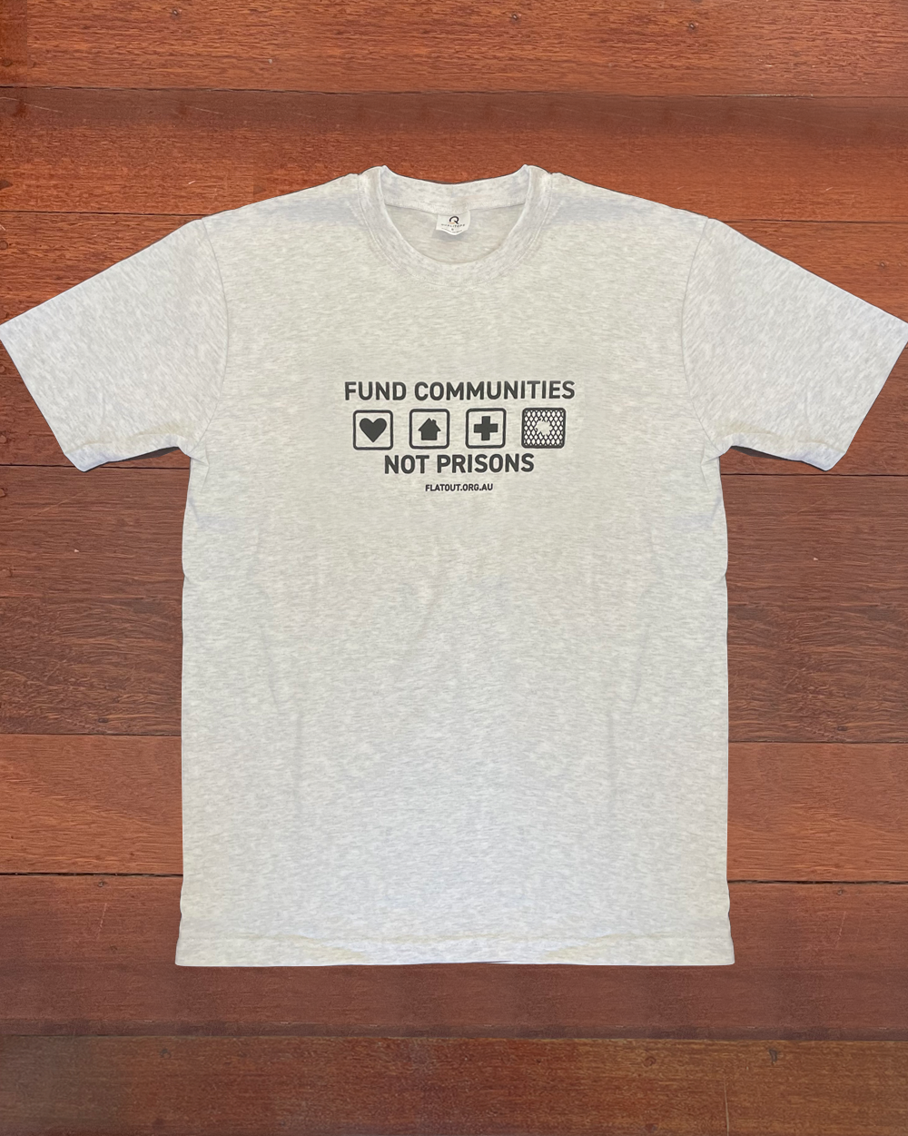 White tshirt with black design on the chest. 4 squares show a heart, a home, a hospital cross and chain wire with a hole in it. Fund communities not prisons. flatout.org.au in small letters.