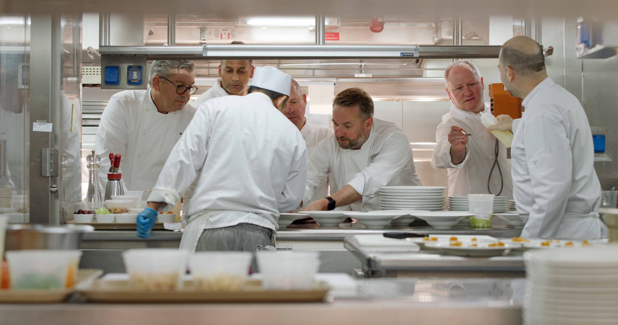 Chefs working in a professional kitchen preparing dishes and plating food.