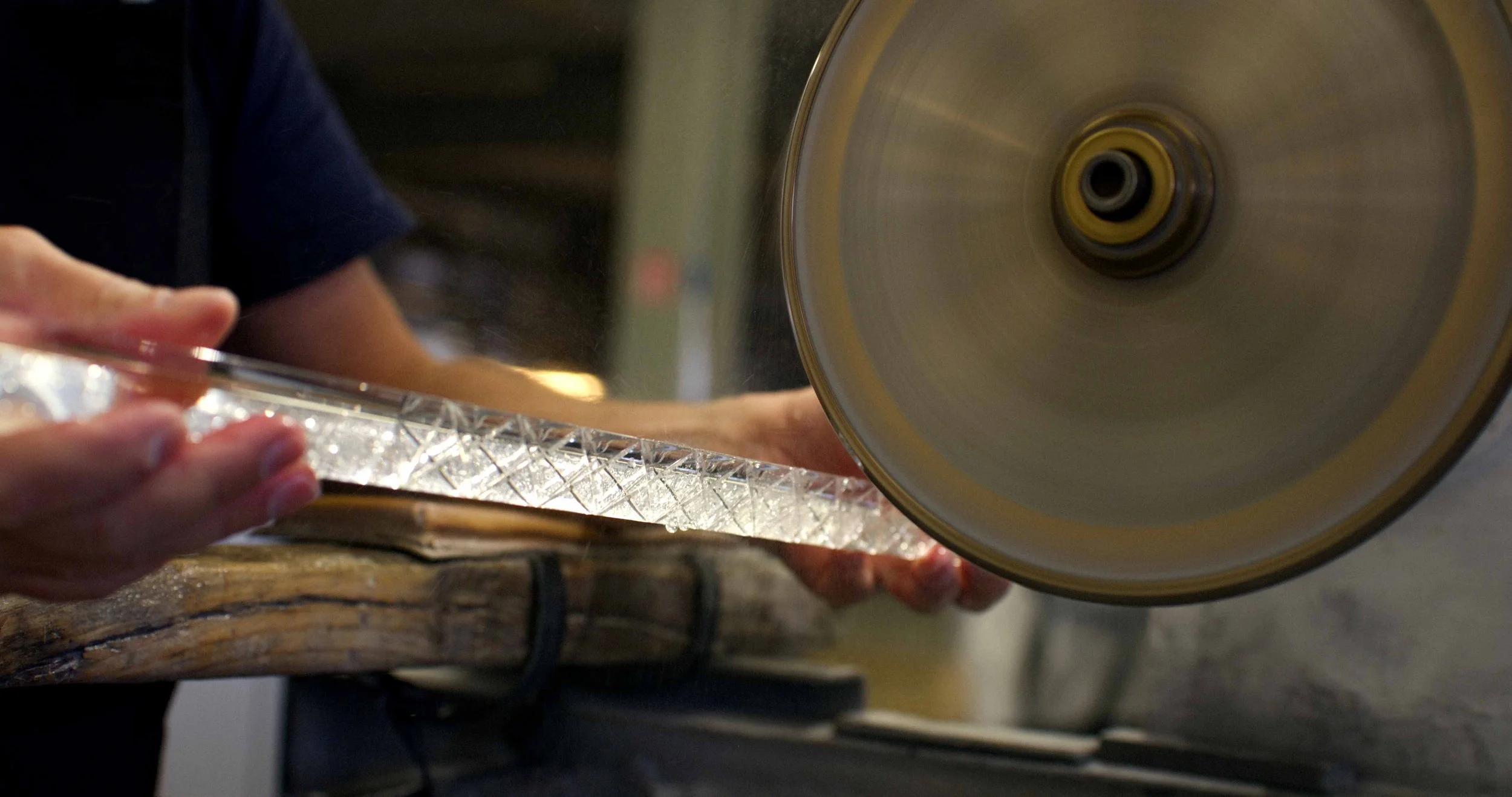 Person cutting glass with a wet saw on a wooden work surface.