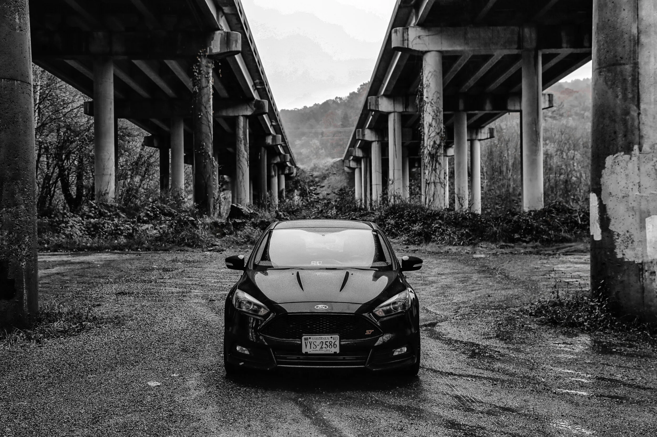 A black Ford Focus ST parked under a highway overpass on a rainy day.