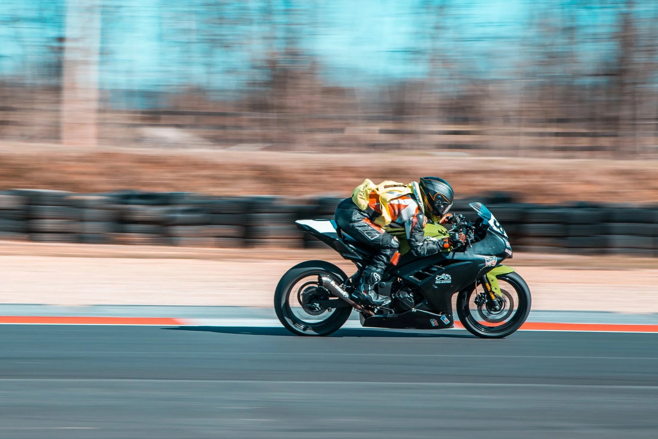 Motorcycle racer in colorful gear leaning into a turn on a racetrack with blurred background.