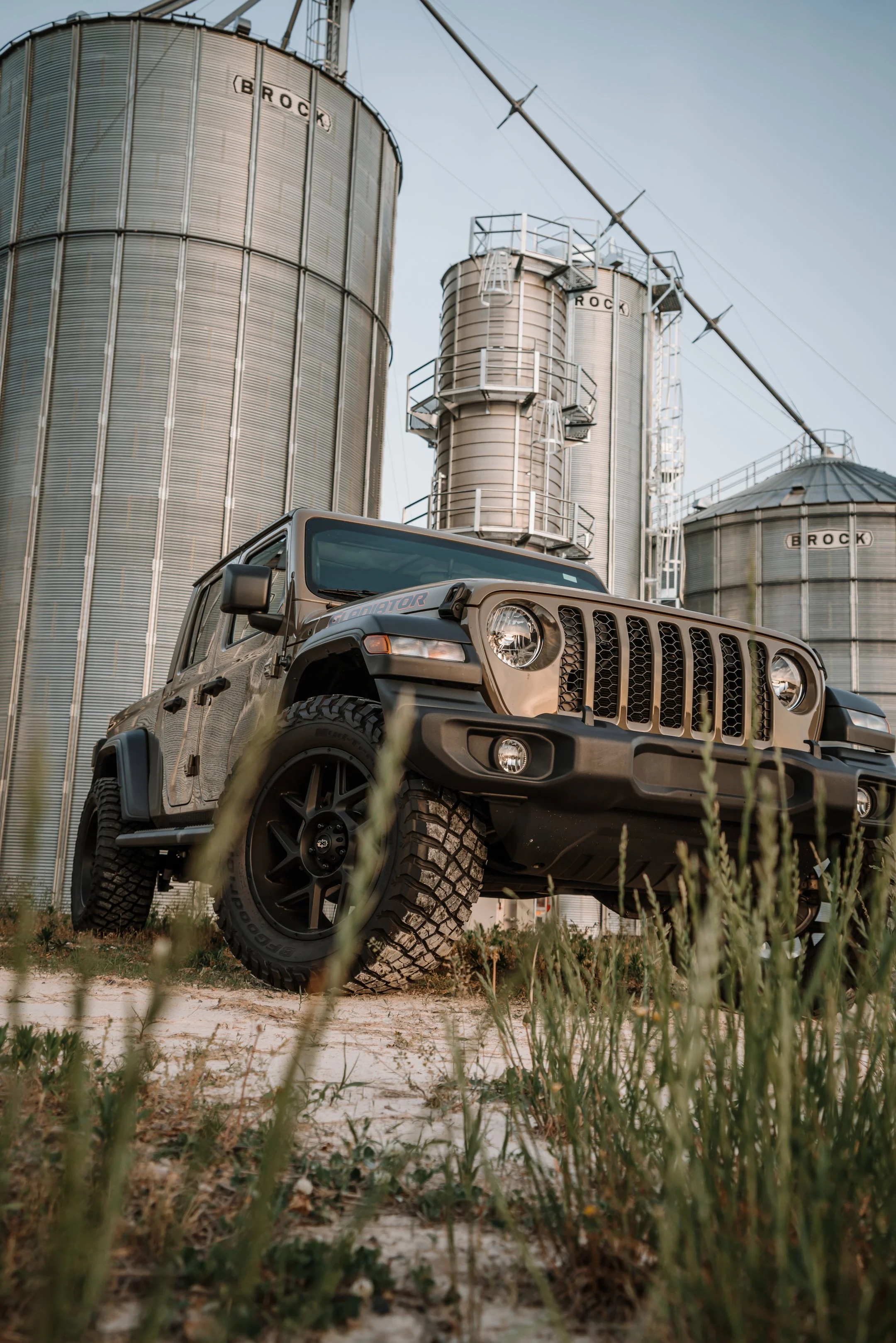 A black Jeep Wrangler Rubicon off-road vehicle parked on grassy terrain with industrial silos in the background.