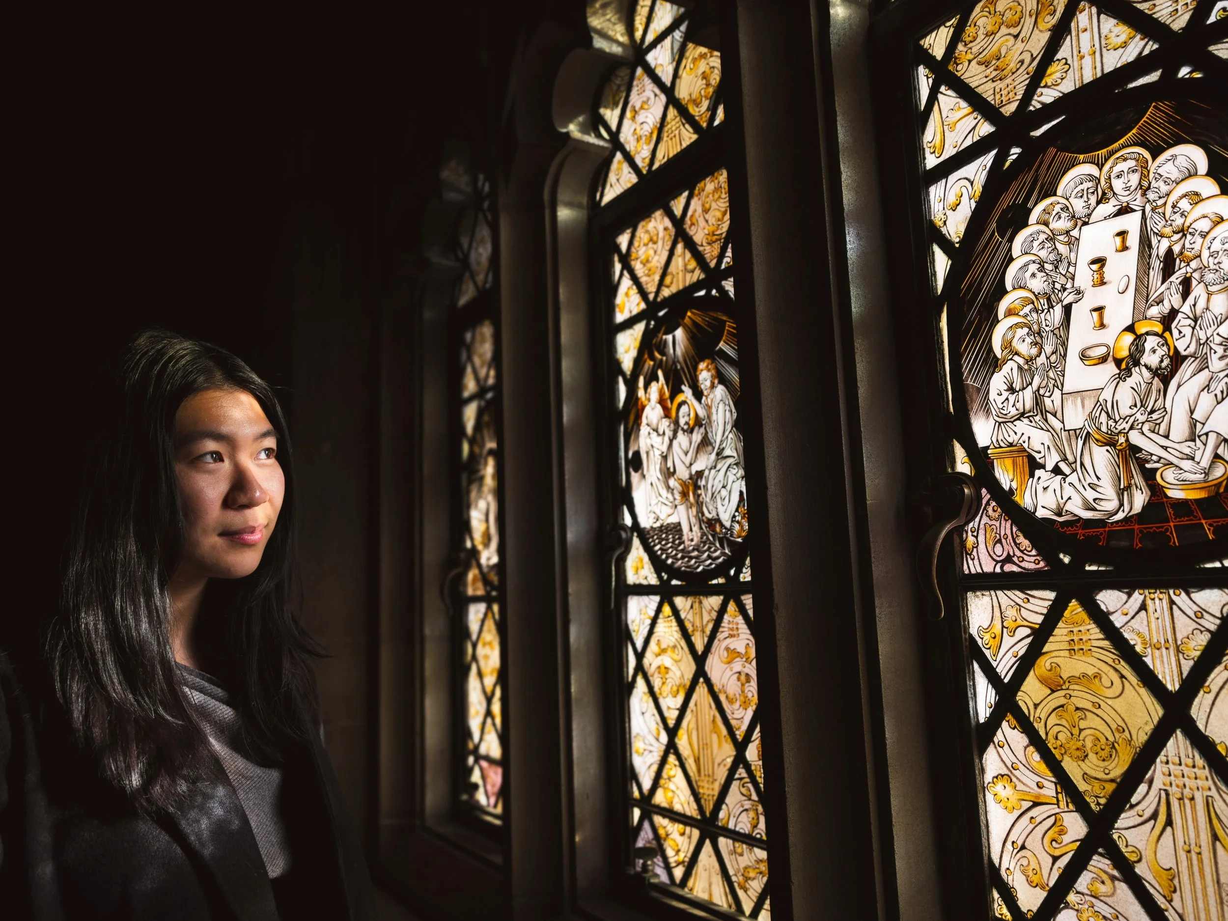 A young woman with long dark hair looking at stained glass windows in a church.
