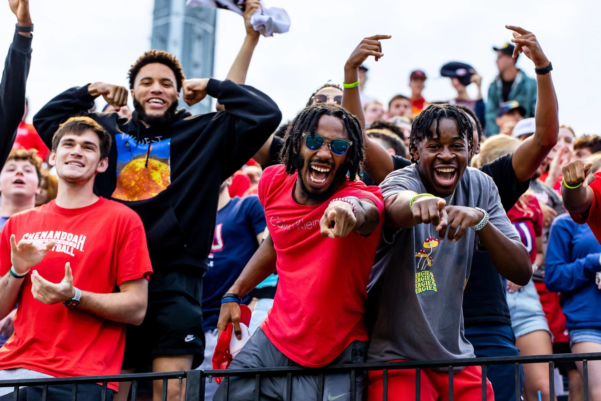 Group of diverse sports fans cheering and celebrating at a stadium, some pointing and smiling enthusiastically.