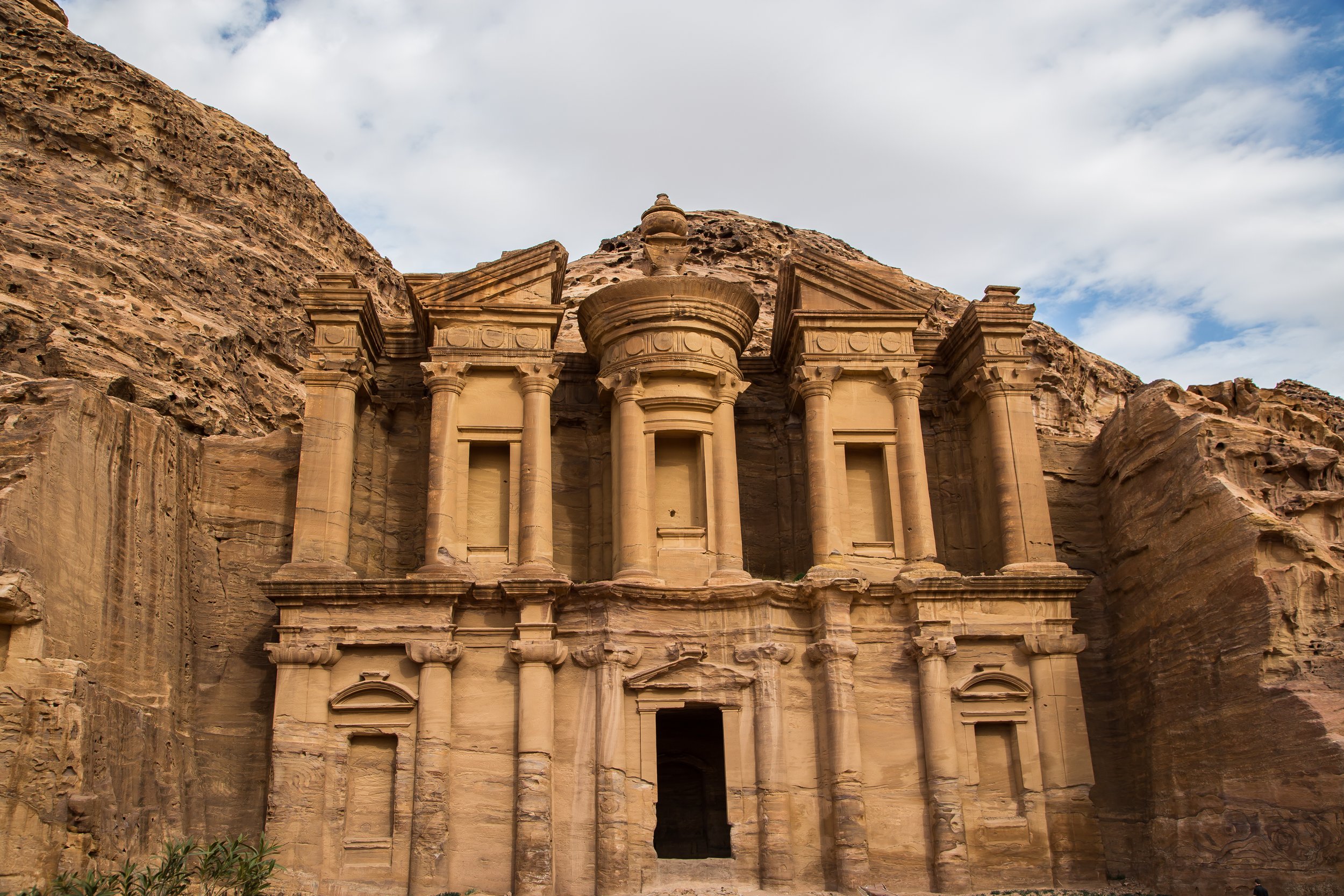 Ancient stone building carved into a cliff face with columns and decorative architecture, resembling a classical or historic structure.