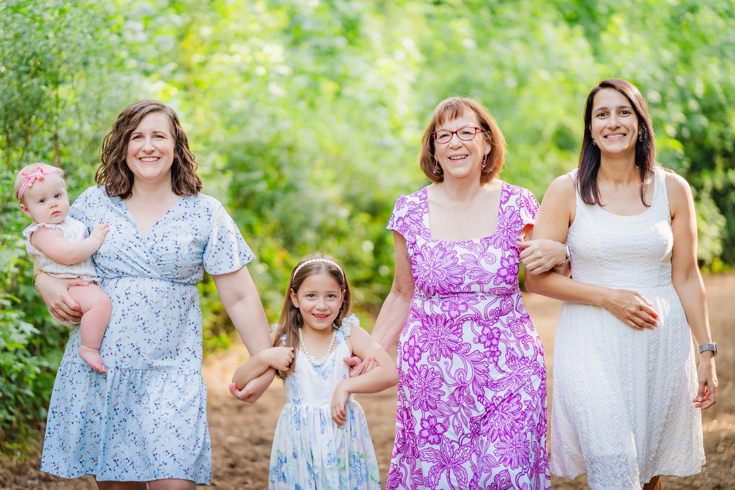 A group of women and young girls walking together outdoors on a sunny day, surrounded by greenery.
