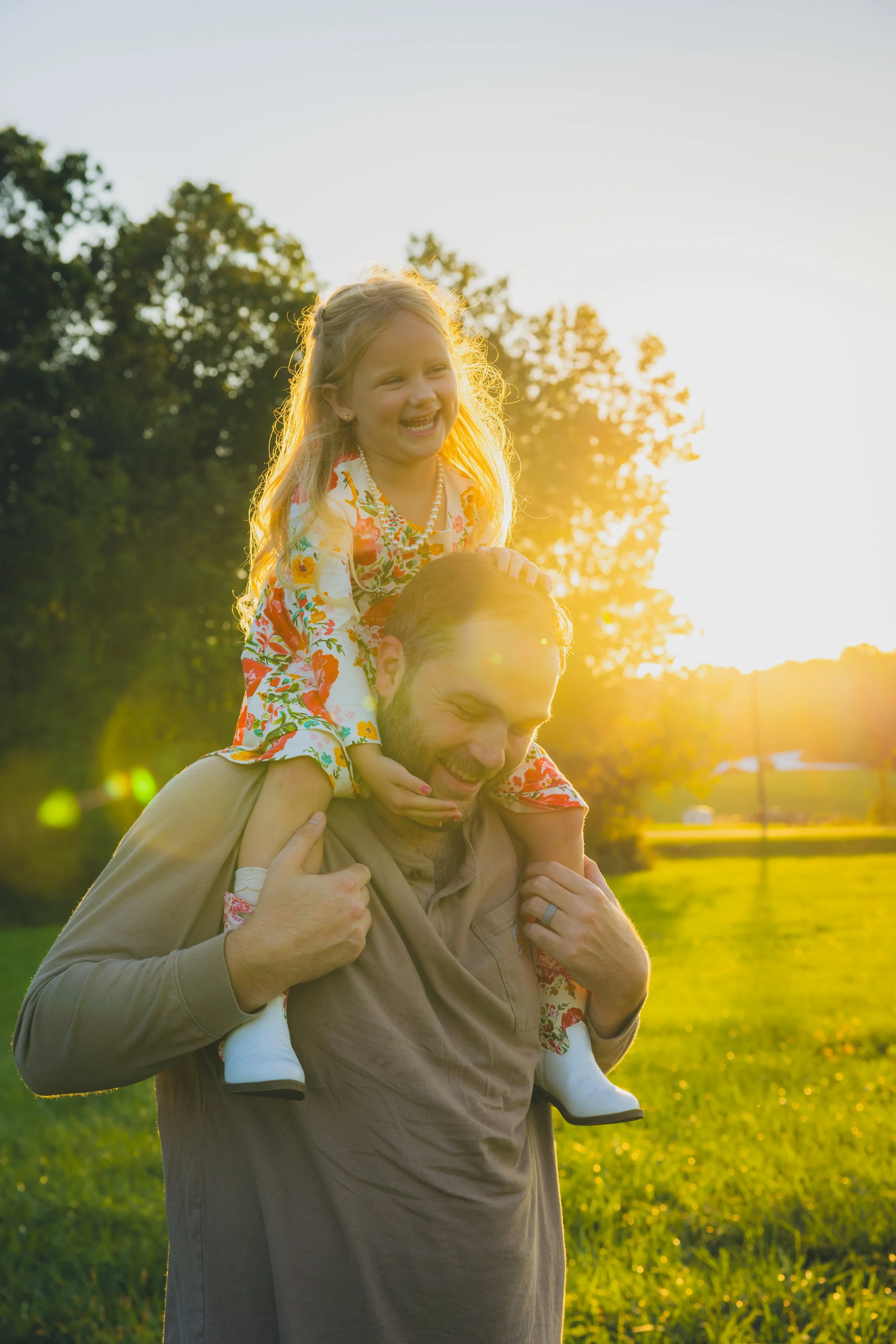 A man giving a piggyback ride to a young girl outdoors during sunset, both smiling and enjoying the moment.