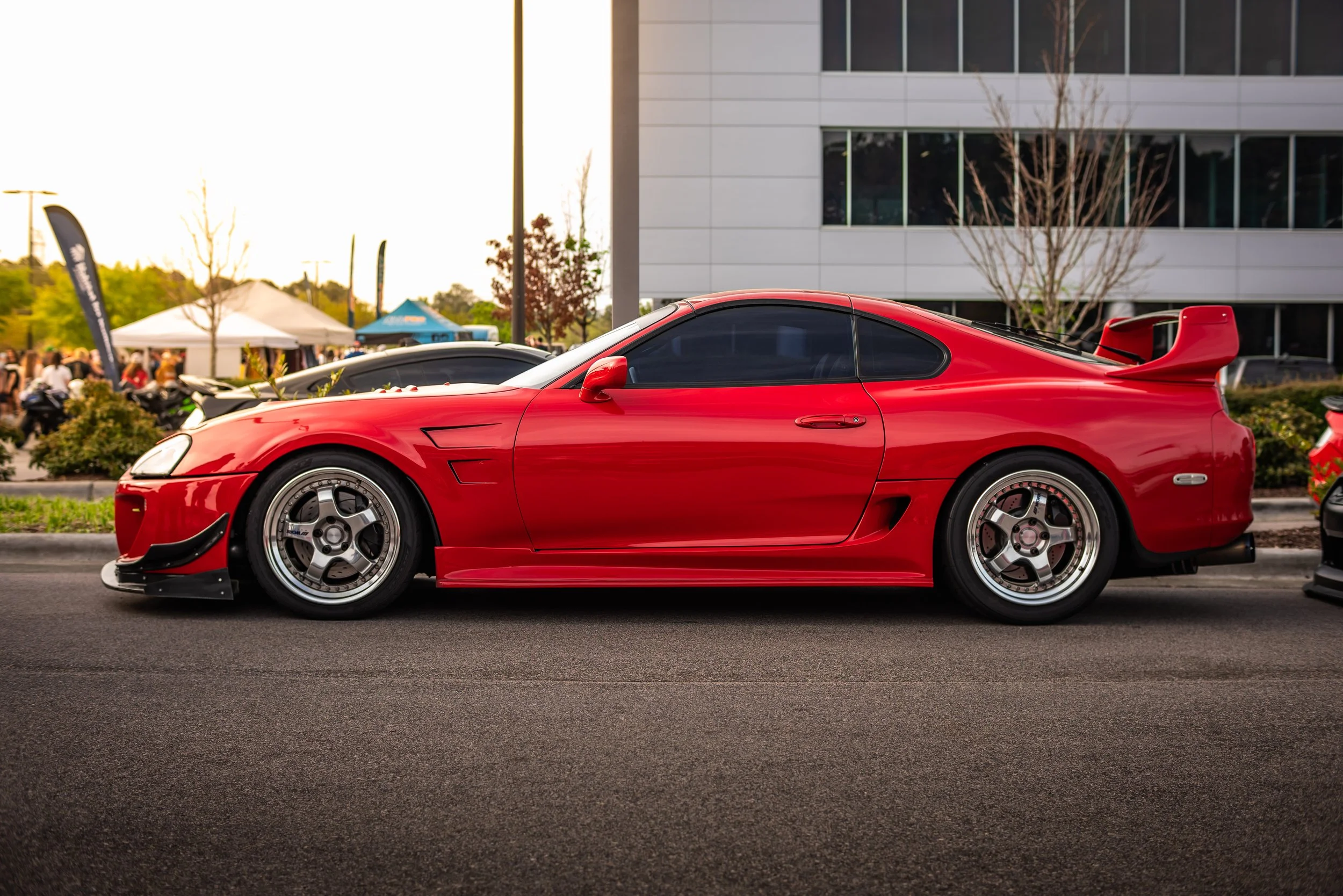 Red sports car parked on the street during daytime, with a building and trees in the background.