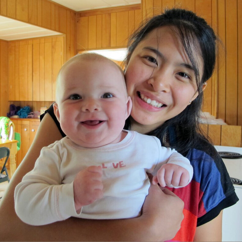 Young PNA Nanny holding smiling baby in kitchen