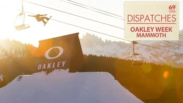 Snowboarder jumping over a large Oakley-branded ramp at a ski resort, with ski lifts in the background and snow-covered mountains under a sunset sky. Text reads 'Dispatches Oakley Week Mammoth.'