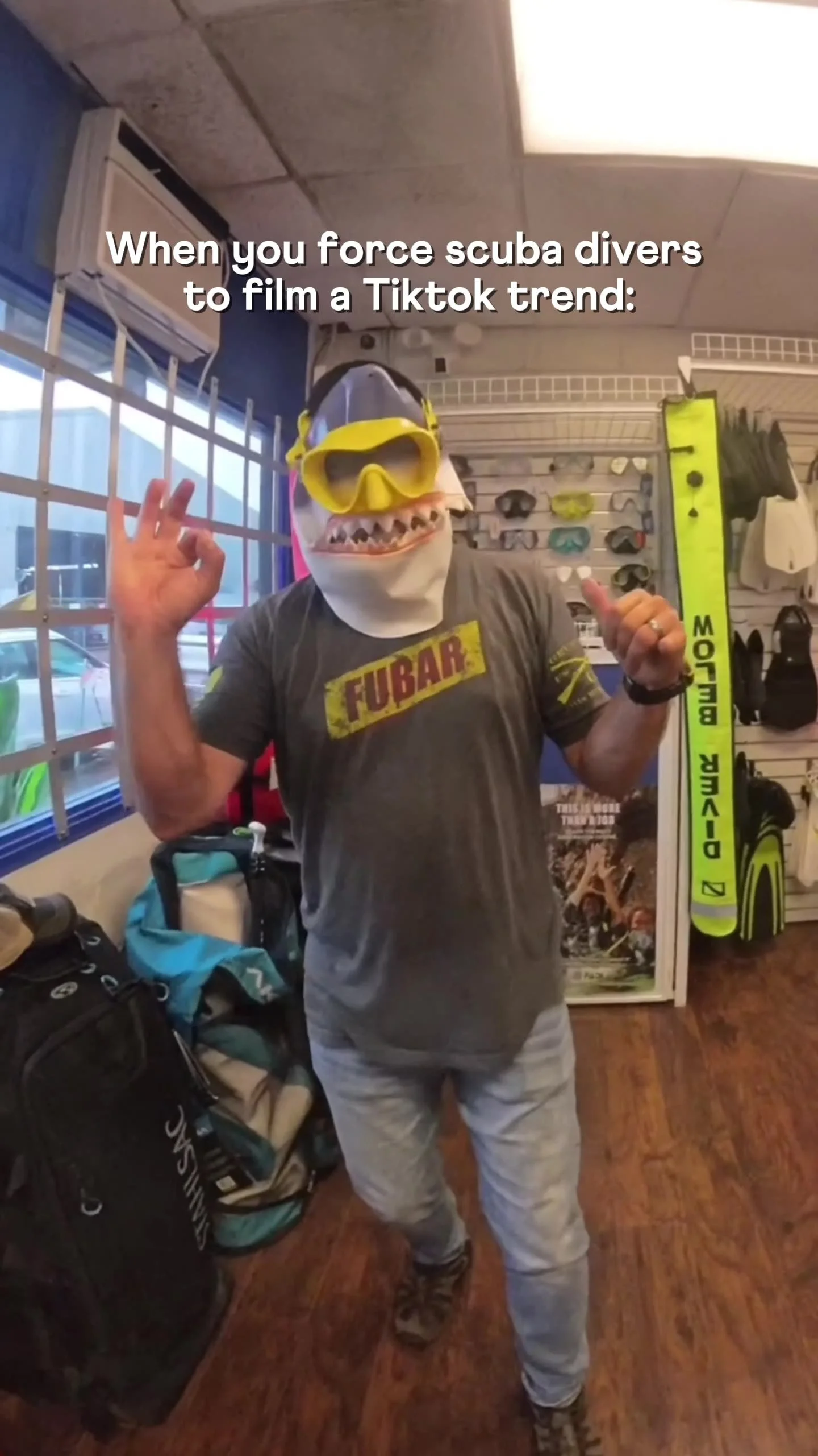 Person wearing a shark mask and scuba gear store, surrounded by hiking and scuba equipment.